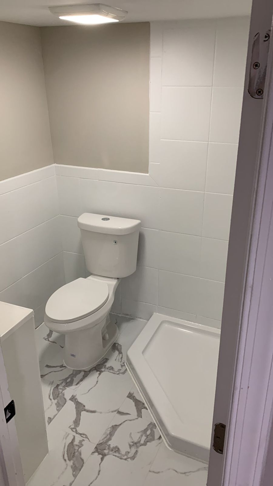 The same basement area rebuilt into a finished bathroom: tiled walls, marble-look porcelain floor, new toilet, shower and exhaust fan.