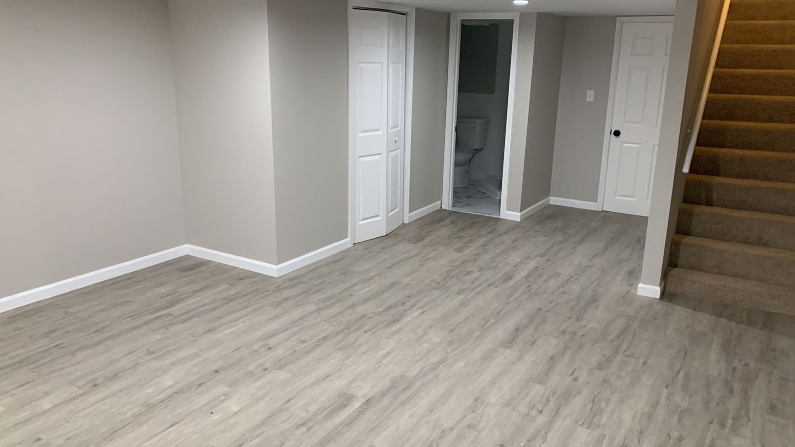 The same Northeast Pennsylvania basement finished, from the same angle: new walls and trim, wood-look vinyl plank flooring, closets and a new bathroom.