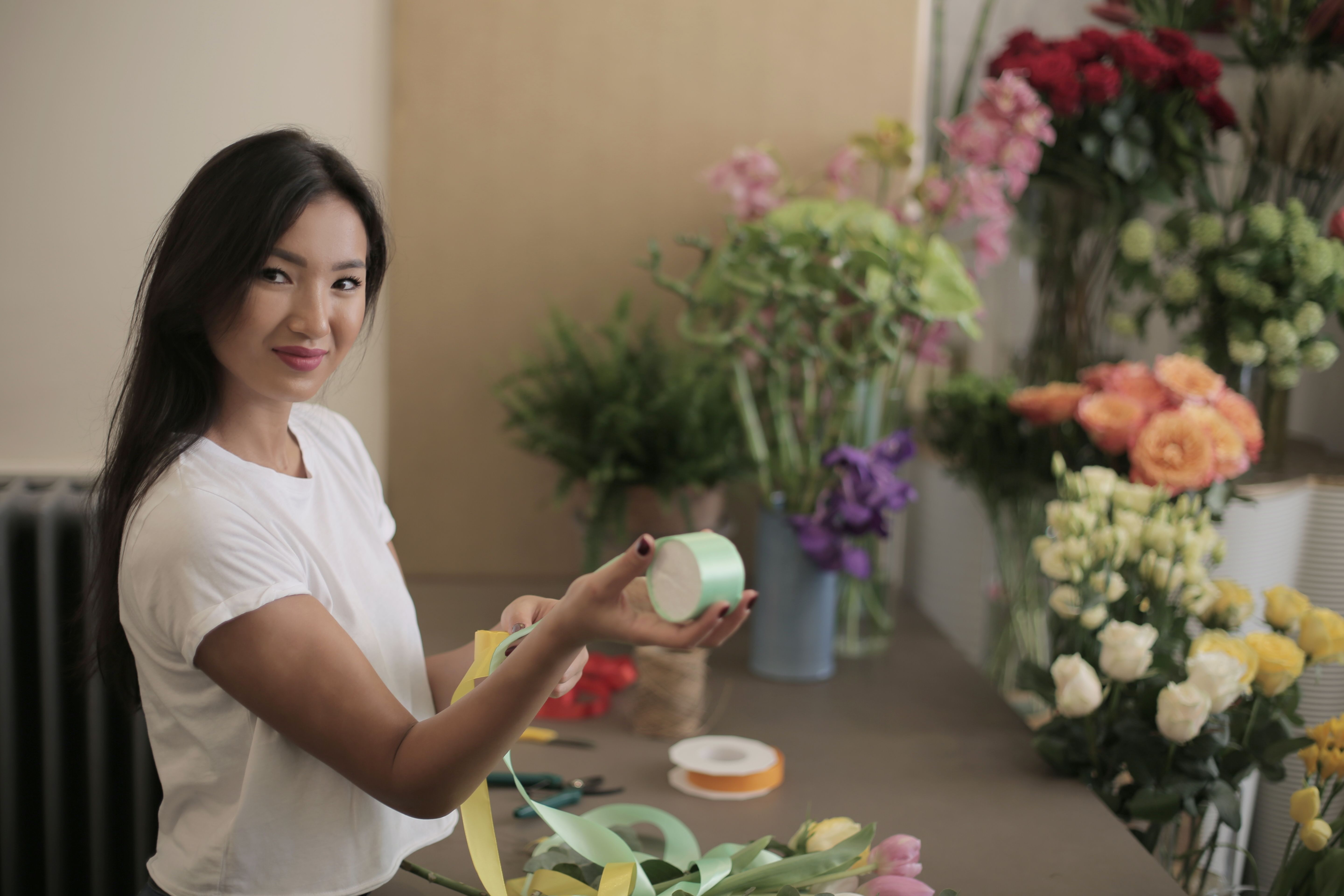 Florist holding colorful ribbons beside flowers in a shop