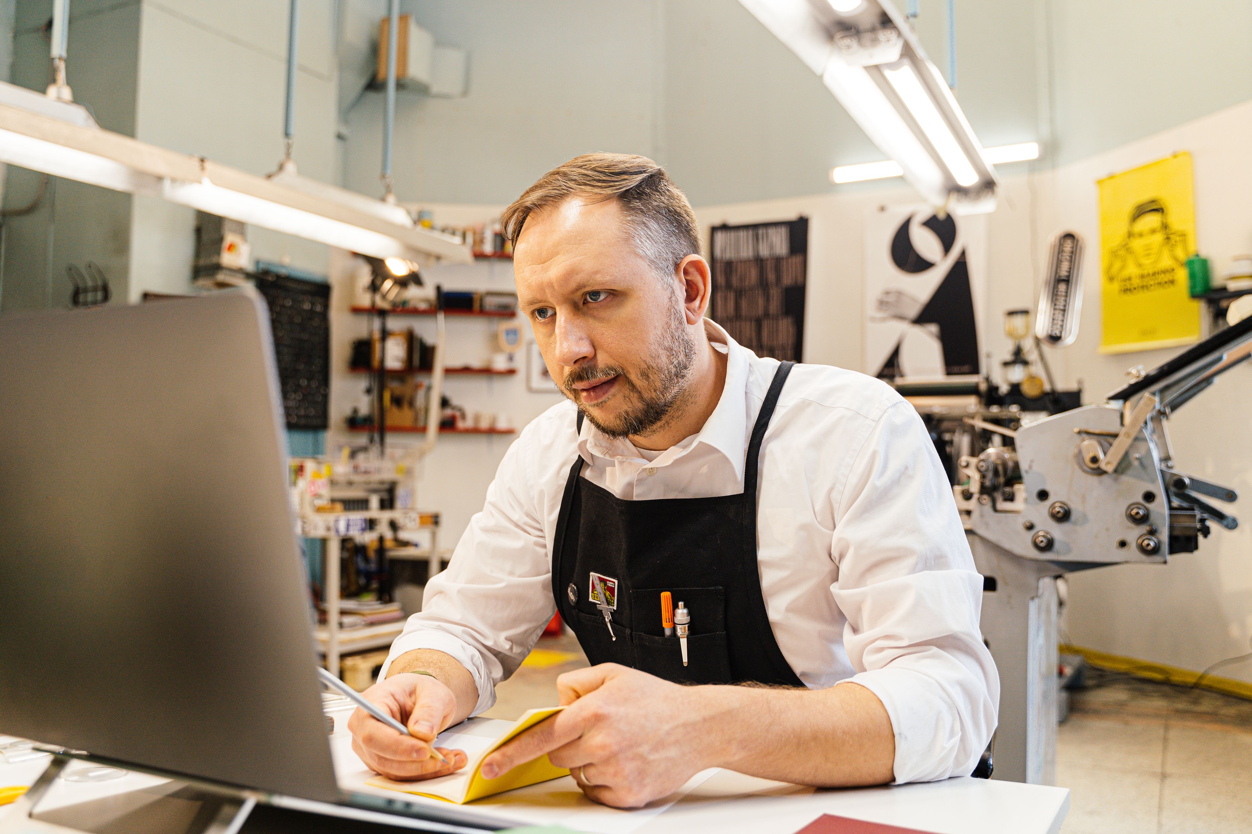 Print-shop professional working at a computer beside printing equipment