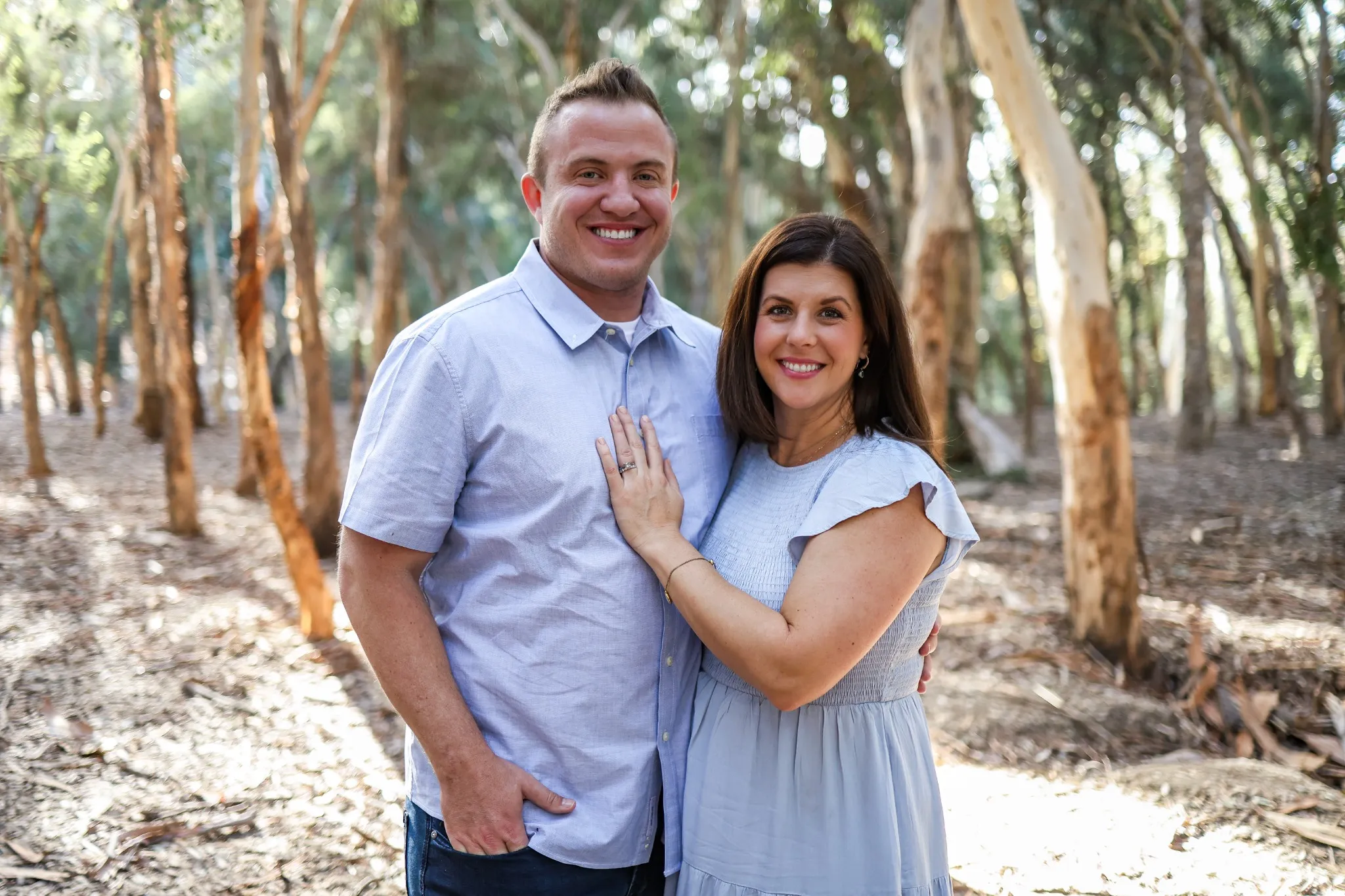 A smiling couple, Sean and Ilissa Cuevas, standing together in a sunlit forest, symbolizing unity, faith, and dedication to building stronger, more compassionate communities.