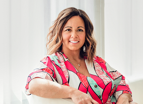 Businesswoman with shoulder-length brunette hair, smiling confidently in a bright patterned blouse.