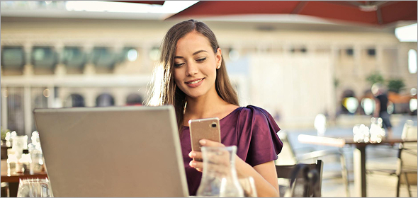 Confident businesswoman working remotely at an outdoor café using her smartphone and laptop