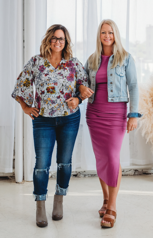 Jessica Green and Natasha Roberson standing together in front of white curtains, dressed in casual-chic outfits with confident, welcoming smiles — showcasing the approachable leadership behind the Self Made brand.