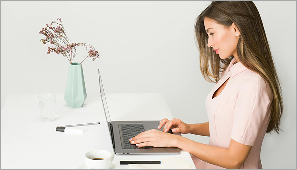 Focused female entrepreneur working on laptop at a clean, modern workspace with a pastel vase