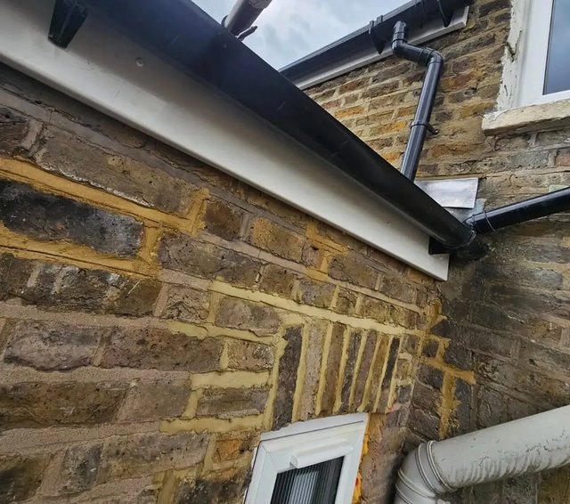Black gutter corner and downpipe with white fascia on a stone building