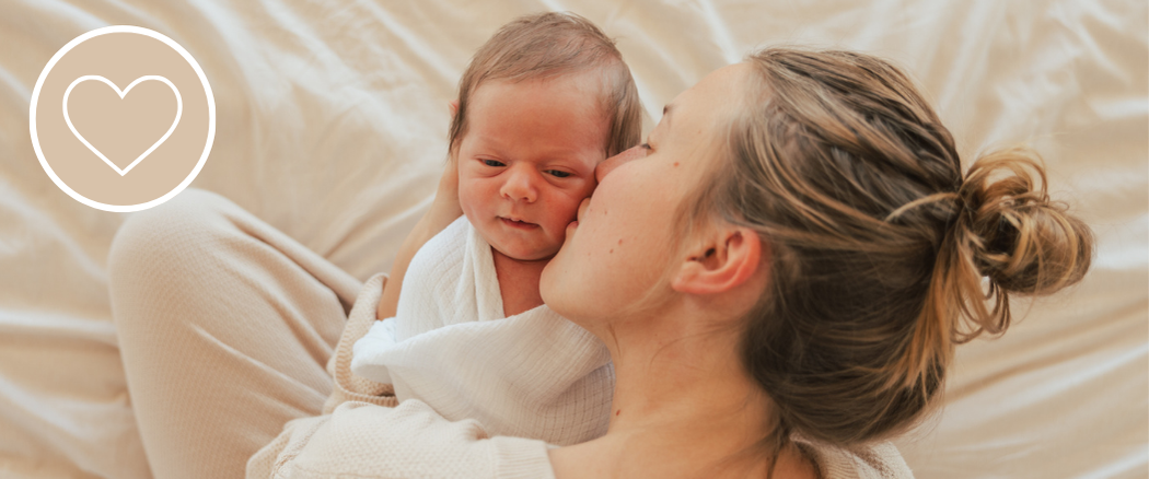 Mother kissing her newborn baby while cuddling in bed.