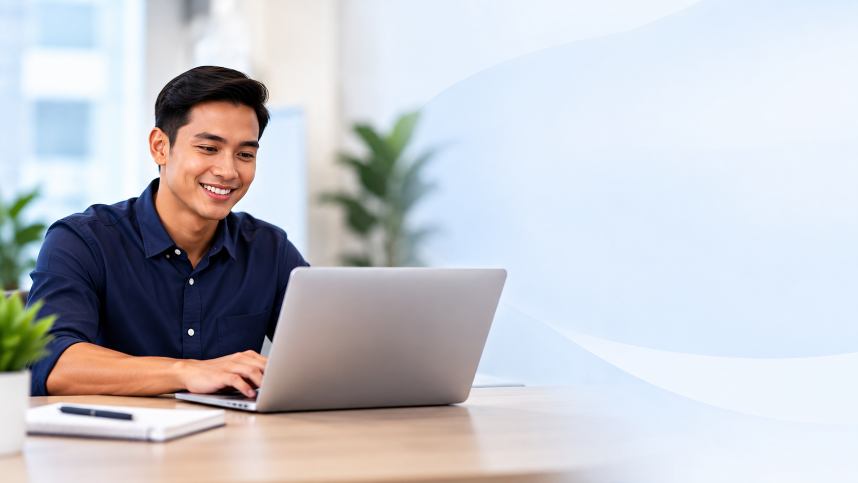 Smiling Filipino professional in a navy shirt typing on a laptop in a bright office