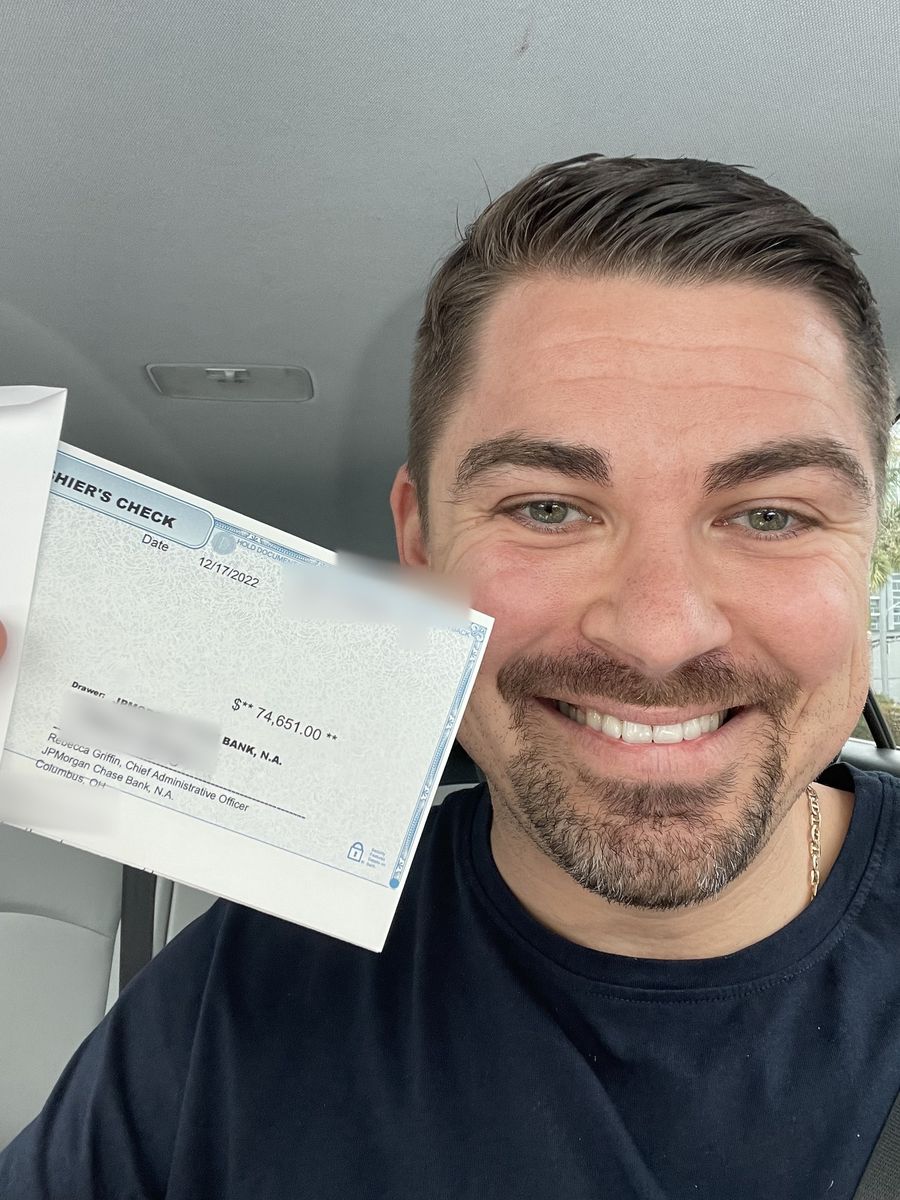 Anton Zherelyev smiling in his car, holding up a cashier's check for $74,651 dated December 17, 2022