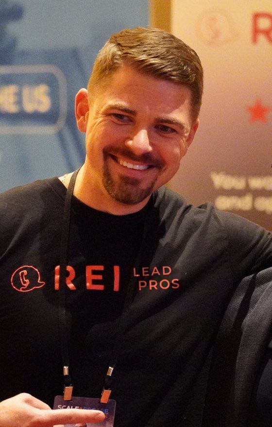 Anton Zherelyev, founder of REI Lead Pros, smiling at an investor event in an REI Lead Pros t-shirt