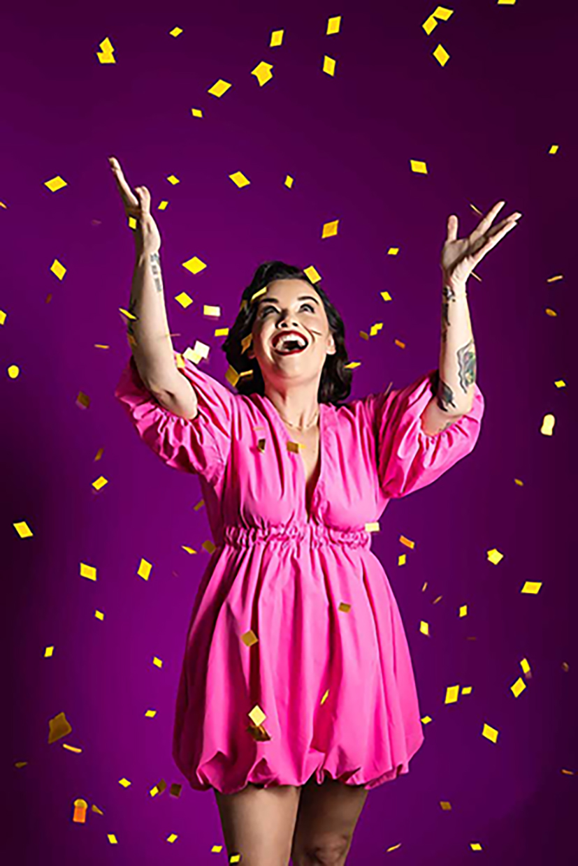 Vibrant studio portrait of joyful woman in a pink dress celebrating with falling gold confetti, bold and colourful fashion photography in Colorado Springs with dynamic expression and playful energy.