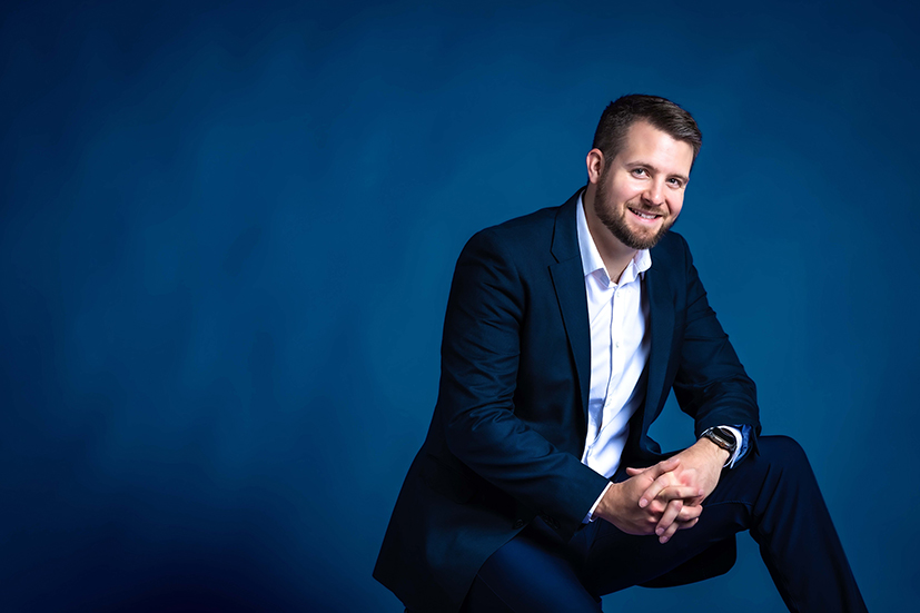 Professional studio headshot of confident businessman in a dark suit and white shirt against a seamless blue background, modern corporate branding portrait in Colorado Springs with clean, contemporary lighting.