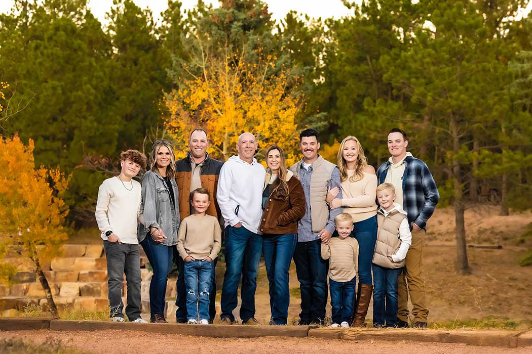 Extended family fall portrait session with multi-generational group posing outdoors in coordinated autumn outfits, warm golden-hour family photography in Colorado Springs forest park with vibrant yellow foliage.