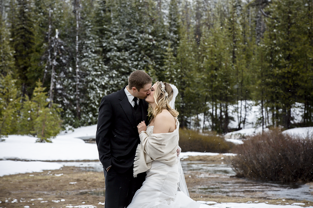 Winter wedding portrait of bride and groom kissing in a snowy forest,  romantic outdoor elopement photography in Colorado Springs with natural pine tree backdrop and seasonal mountain ambiance.