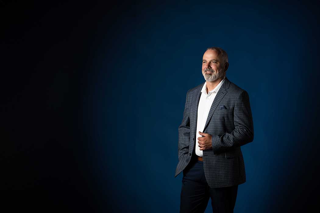Confident professional headshot of mature businessman in checkered blazer and white shirt against a deep blue studio background, modern executive portrait in Colorado Springs with clean lighting and corporate style.