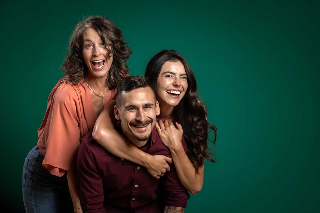 Joyful group studio portrait of three smiling adults against a green backdrop, fun and candid lifestyle photography in Colorado Springs capturing real connection and expressive personality.