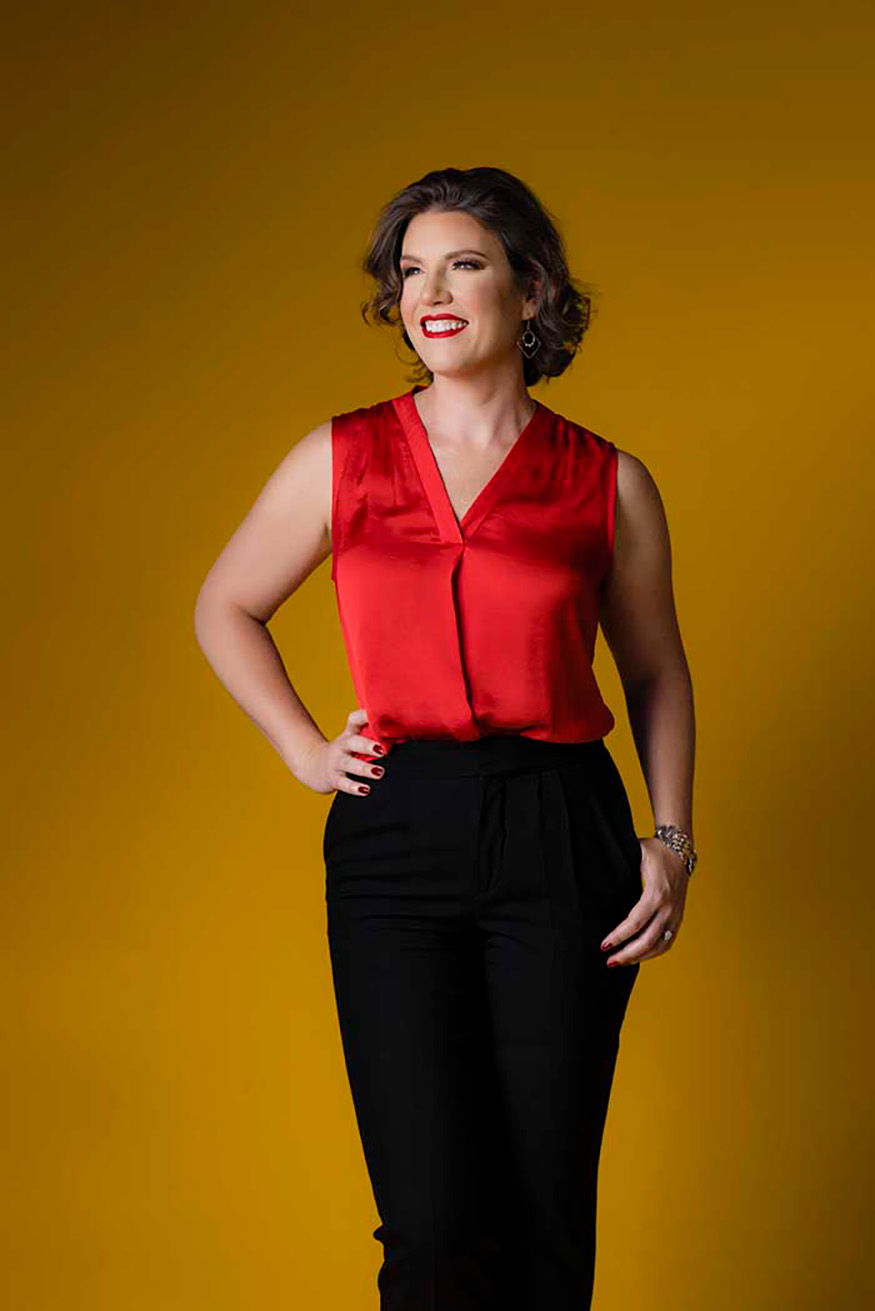 Confident businesswoman in red sleeveless blouse and black trousers smiling against a golden yellow studio background, modern personal branding portrait in Colorado Springs with bold color and professional elegance.