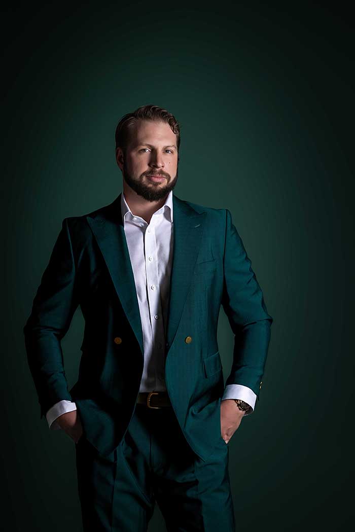 Confident male professional in a dark green tailored suit posing against a rich green studio backdrop, modern executive portrait in Colorado Springs for branding, business, or editorial use.