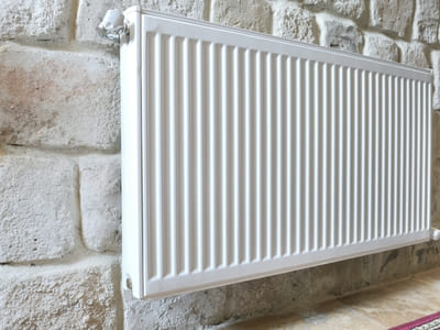 Close-up of a white radiator mounted on a stone wall, part of a home heating system.