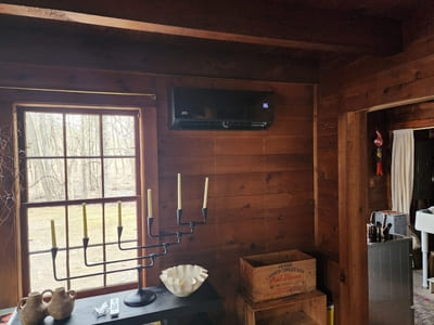 Wall-mounted air conditioning unit installed in a wood-paneled room, maintaining comfortable indoor temperatures.