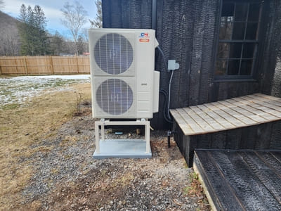 Outdoor heat pump unit installed beside a black wooden house, offering efficient heating and cooling.