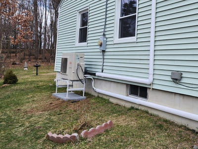 Outdoor heat pump unit installed on the side of a light green house, providing energy-efficient heating and cooling.