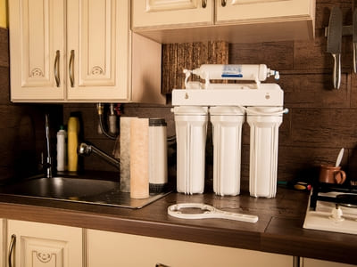 Under-sink water filtration system with multiple stages of filtration, installed in a kitchen for clean drinking water.