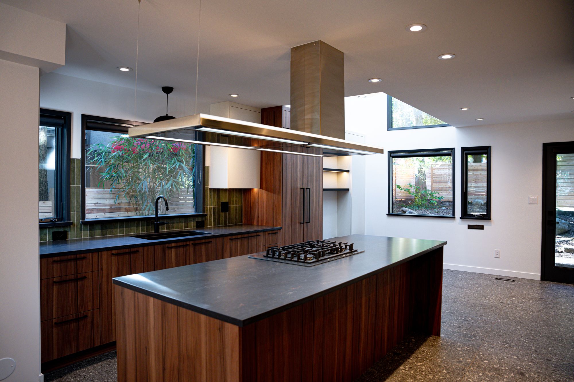 Open-concept kitchen renovation with walnut island, linear pendant light and stainless hood under a skylight