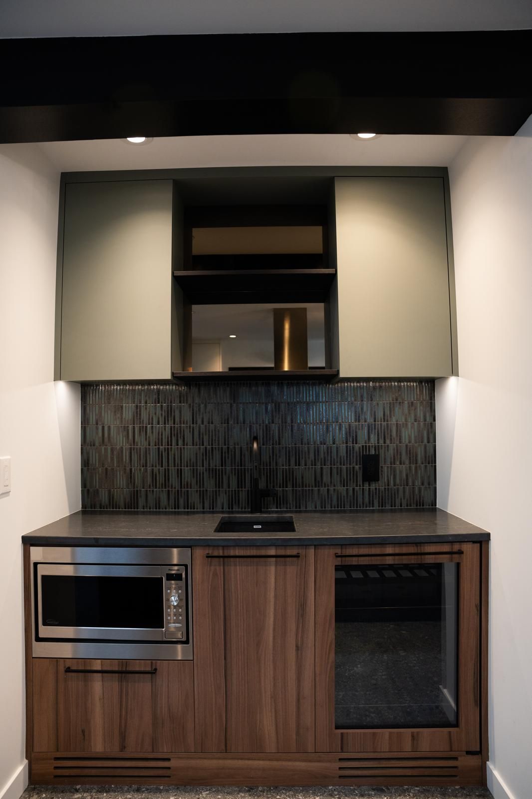 Kelar Homes renovation with walnut kitchenette cabinets, built-in microwave, wine fridge and dark tile backsplash