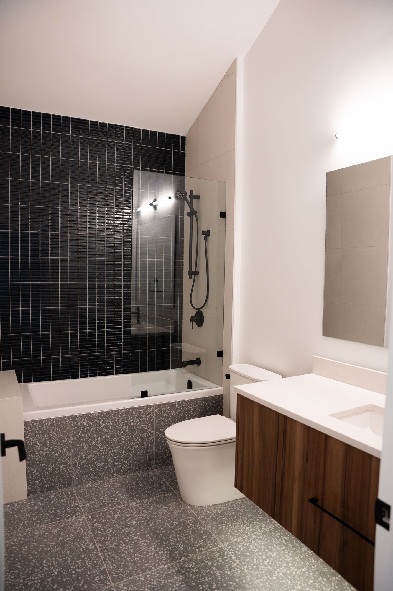 Bathroom renovation with black tile tub surround, walnut vanity and terrazzo-style floor