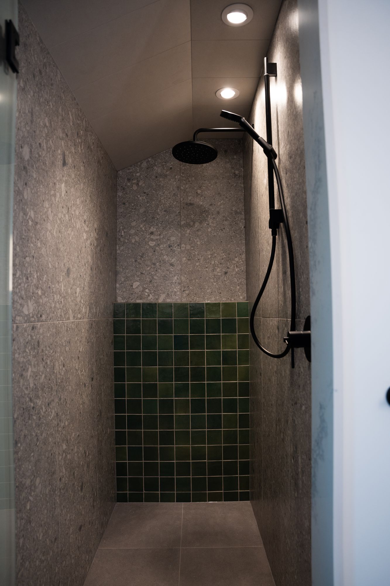 Walk-in shower with green tile, terrazzo walls and matte black rain shower
