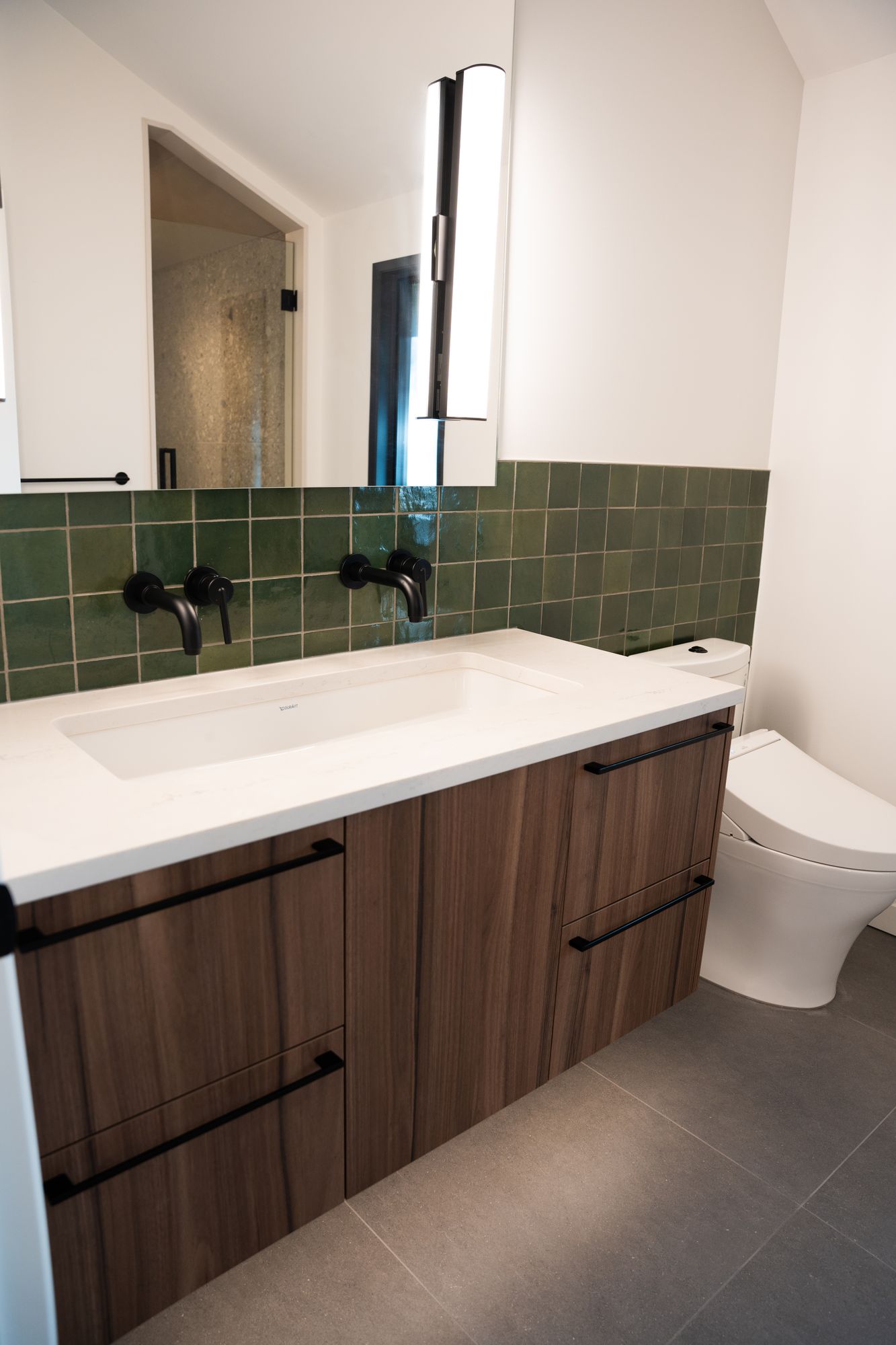 Bathroom renovation with long white trough sink, walnut drawers and green tile backsplash