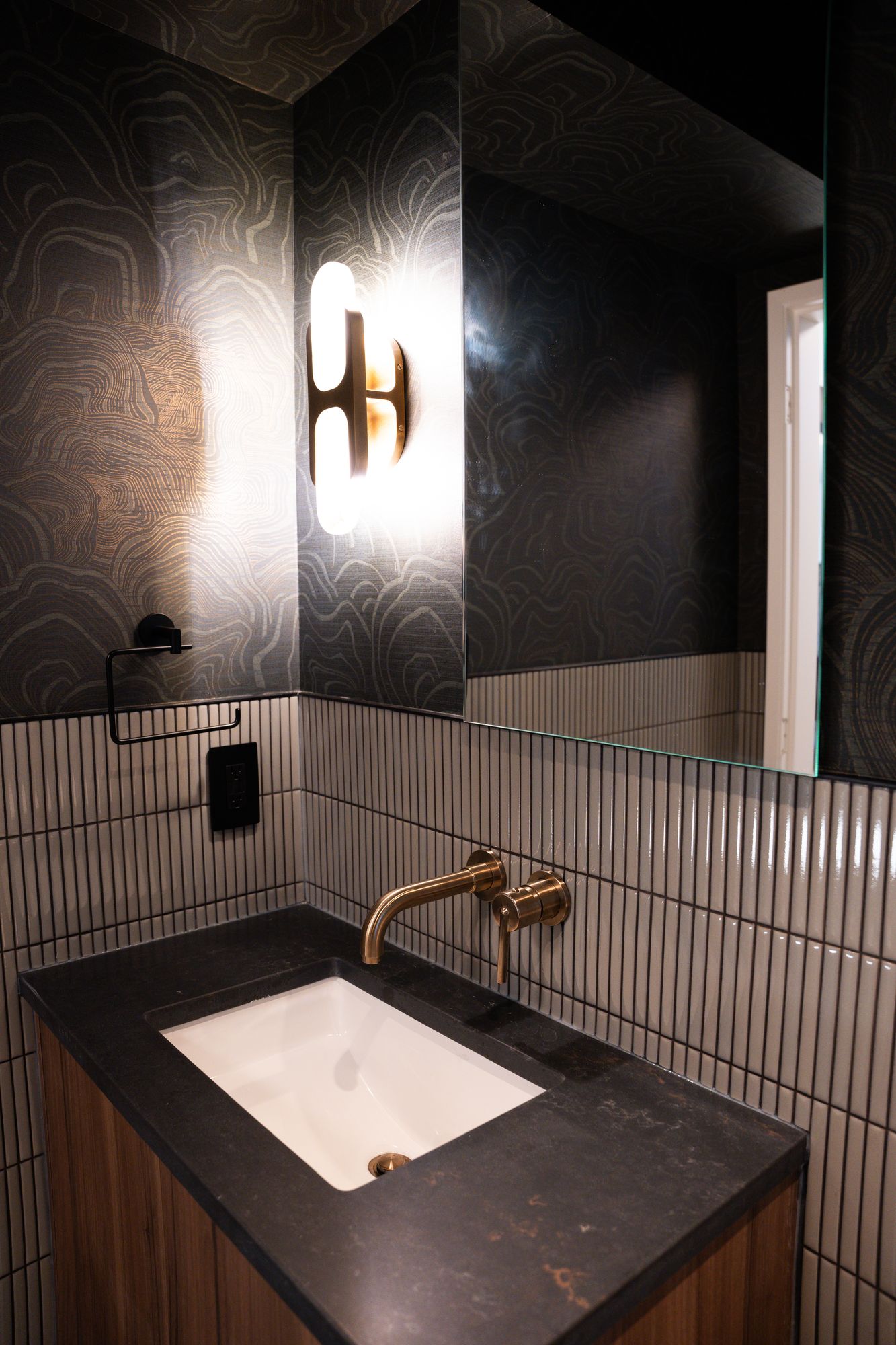 Powder room vanity with black stone counter, undermount sink, brass faucet and vertical tile