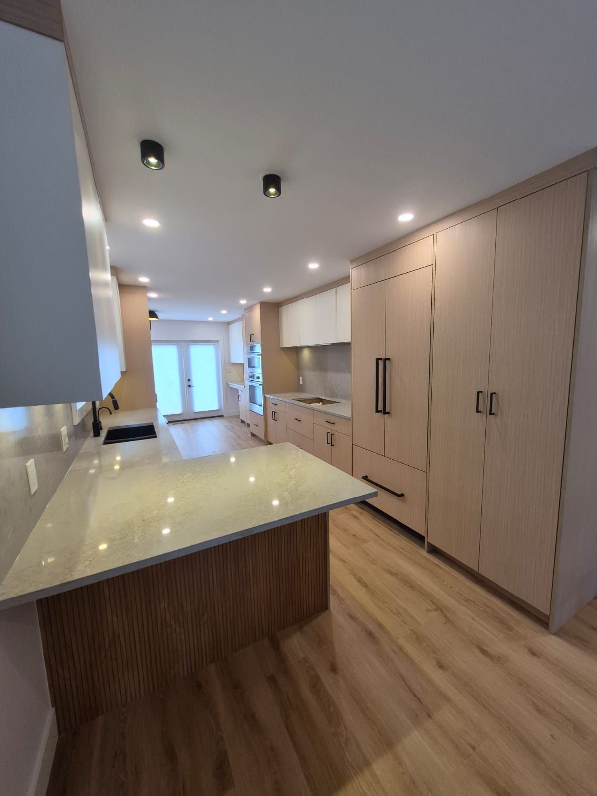 Kitchen renovation with quartz island and light wood floor-to-ceiling cabinets