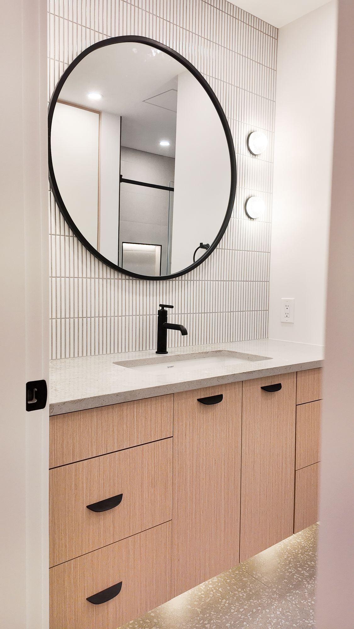 Bathroom vanity with round black mirror, light wood drawers and under-vanity lighting