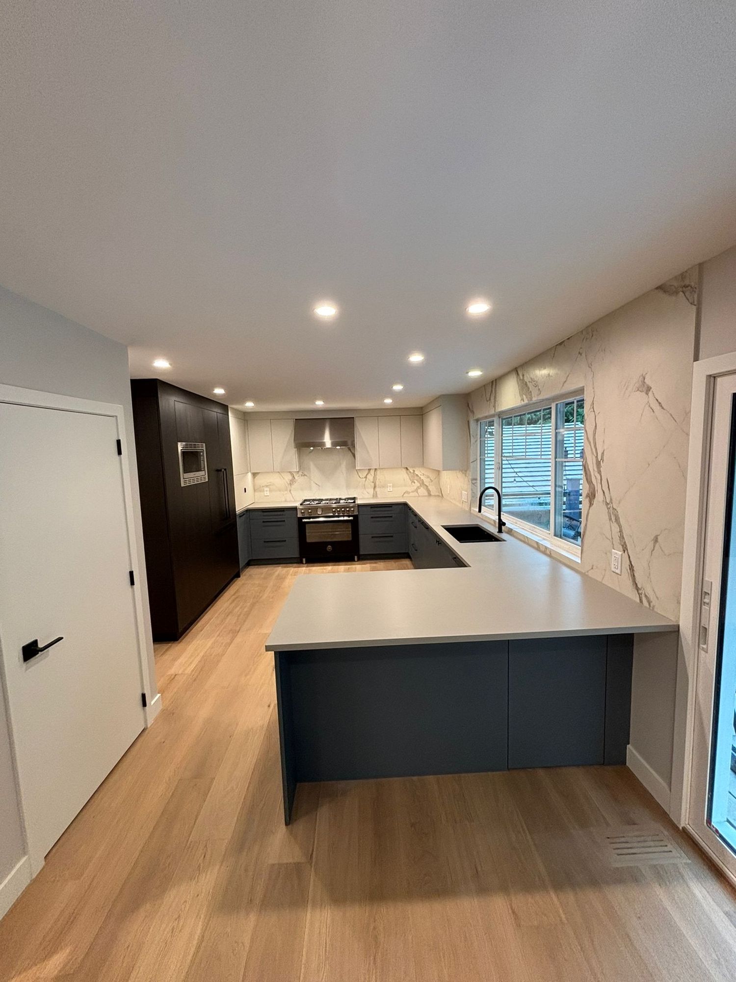 Kitchen renovation with navy peninsula, white quartz counters and wide-plank floors
