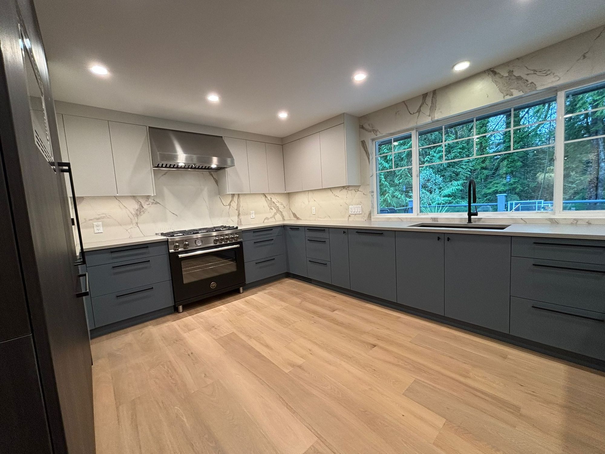 Kitchen renovation with navy lower cabinets, marble backsplash and large windows