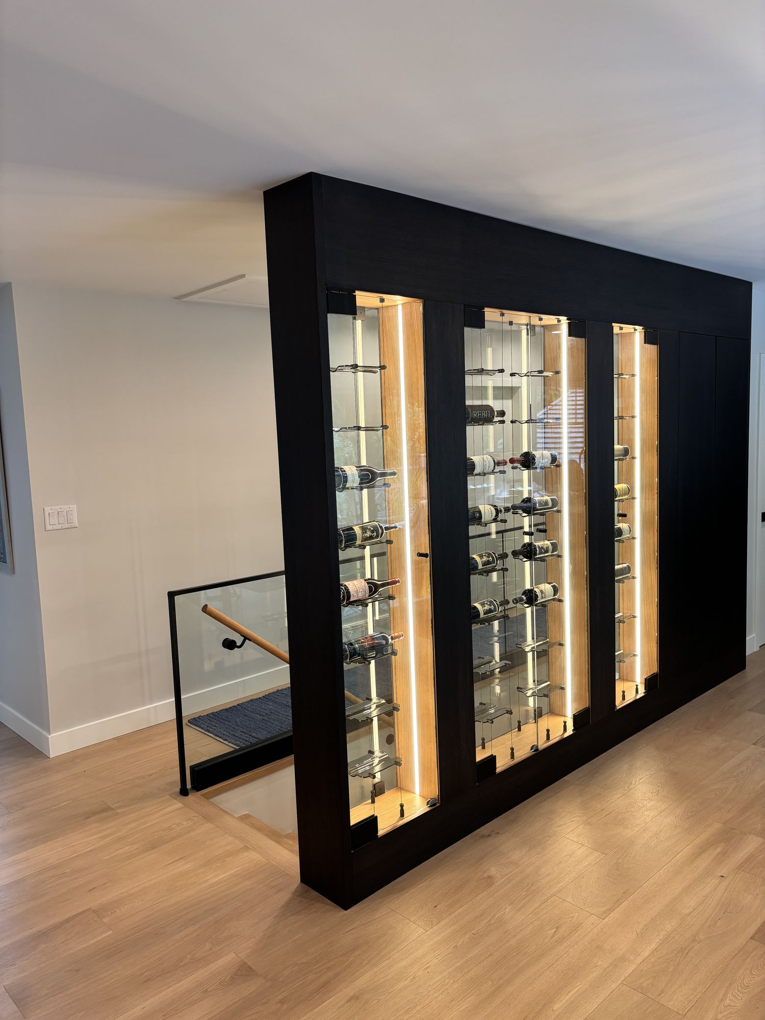 Freestanding black wine cellar with LED-lit glass doors at the top of the stairs