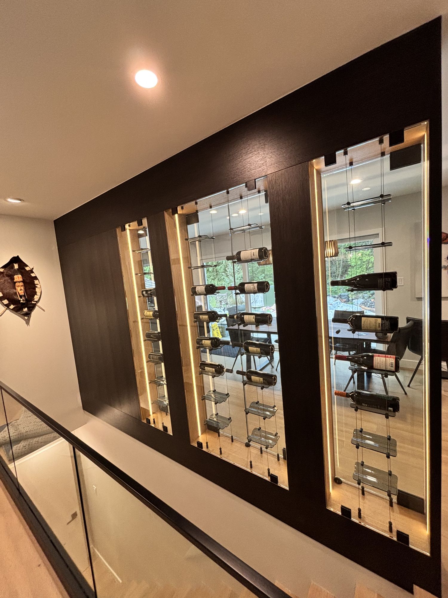 Custom wine cellar with lit glass-front bottle displays beside a glass stair railing