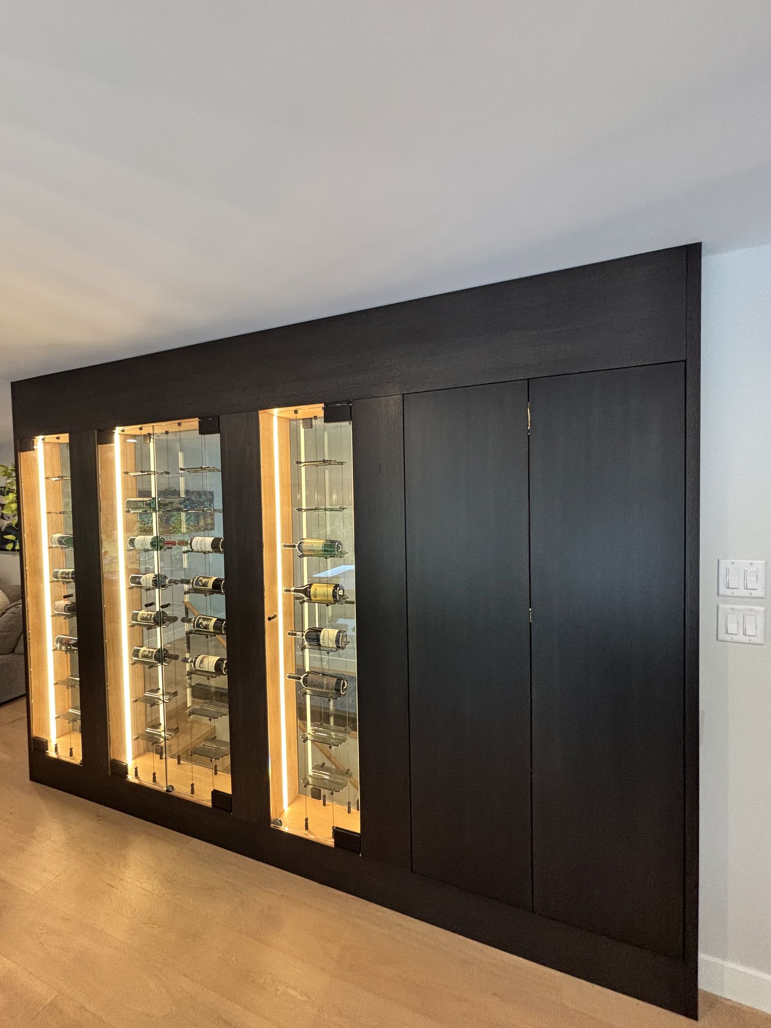 Built-in black wine cellar wall with illuminated glass bottle displays
