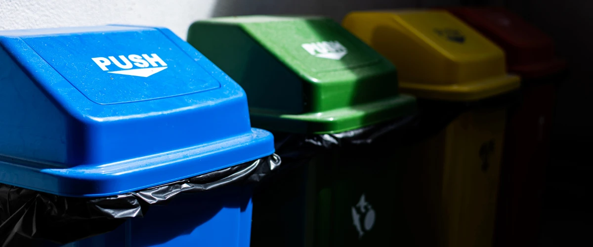 Row of blue, green, yellow, and red recycling bins for waste separation.