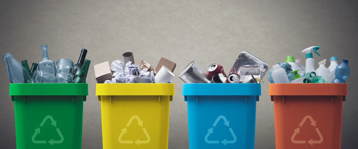 Recycling bins filled with glass bottles, paper, cans, and plastic containers.