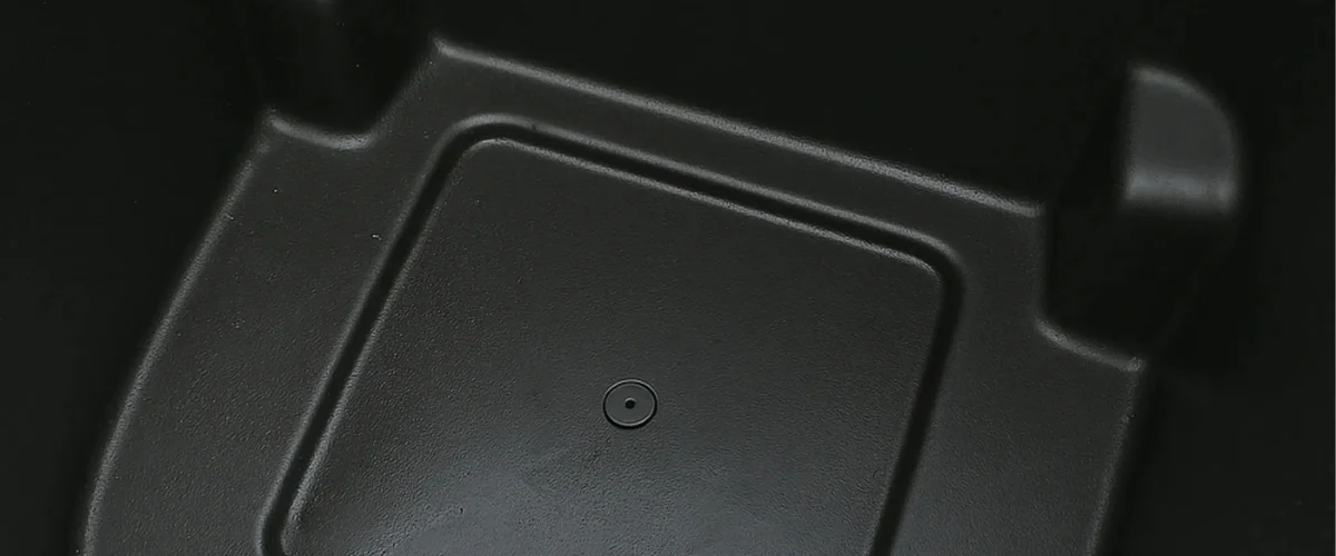 A close-up, high-angle shot showcasing a deep black, textured plastic surface with a subtle circular indentation.