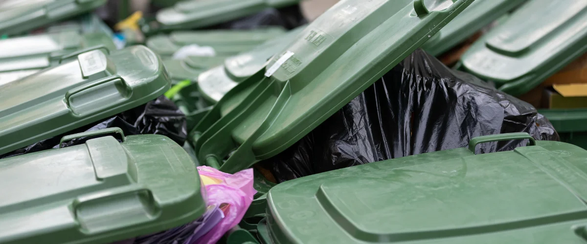 A close-up view of multiple green dumpster lids and black trash bags overflowing with waste.