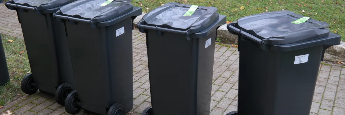 Four gray wheeled garbage bins lined up on paved area. Four gray wheeled garbage bins lined up on paved area.