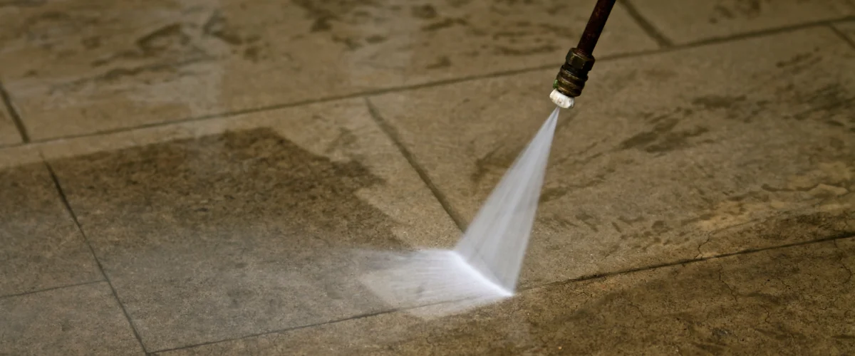 A person in yellow boots and blue pants power washing a stone patio surrounded by decorative rocks and plants. A person in yellow boots and blue pants power washing a stone patio surrounded by decorative rocks and plants.
