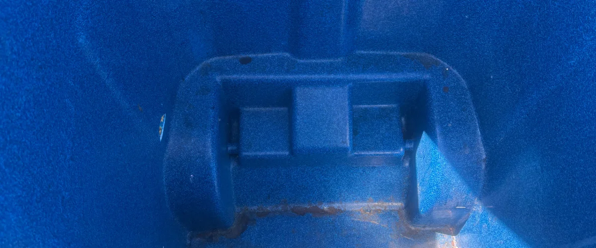 A close-up, high-angle view of the textured blue plastic interior of a bin, showing structural details and a rusty bottom. A close-up, high-angle view of the textured blue plastic interior of a bin, showing structural details and a rusty bottom.