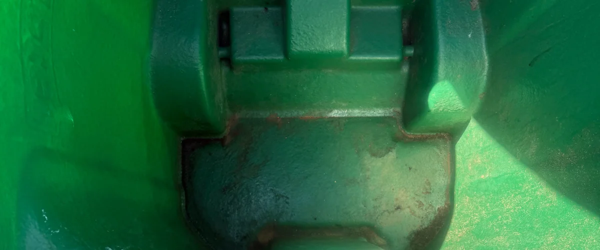 A close-up, overhead view of a dark green metal machinery joint with visible wear and tear, and lighter green surrounding panels. A close-up, overhead view of a dark green metal machinery joint with visible wear and tear, and lighter green surrounding panels.