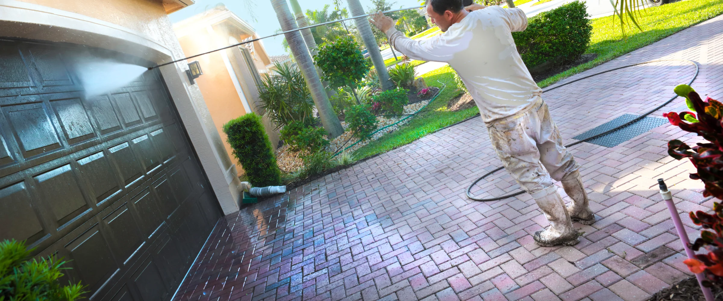 A man pressure washing a dirty concrete driveway, creating a clean wet strip next to dry, grimy pavement. A man pressure washing a dirty concrete driveway, creating a clean wet strip next to dry, grimy pavement.