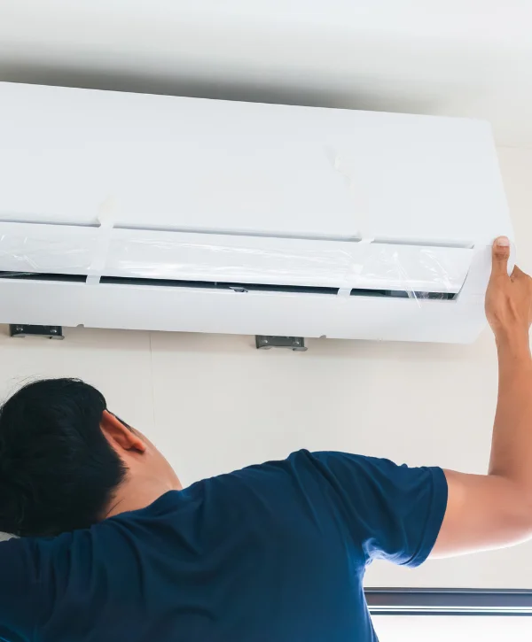 A man in a navy blue shirt installing a new white air conditioner unit on a light-colored wall.